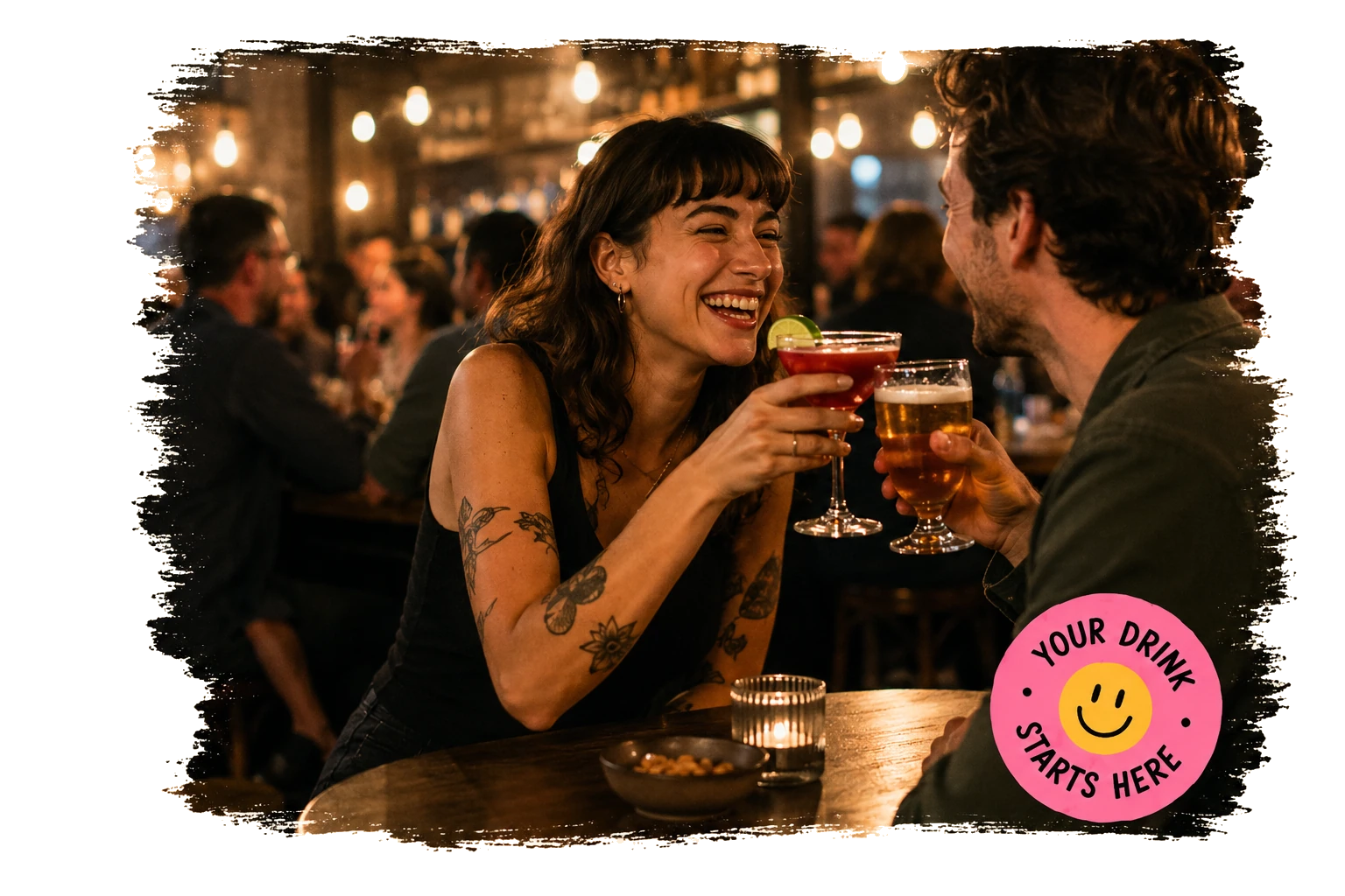 Friends laughing and toasting a cocktail and a beer together in a warm, lively bar